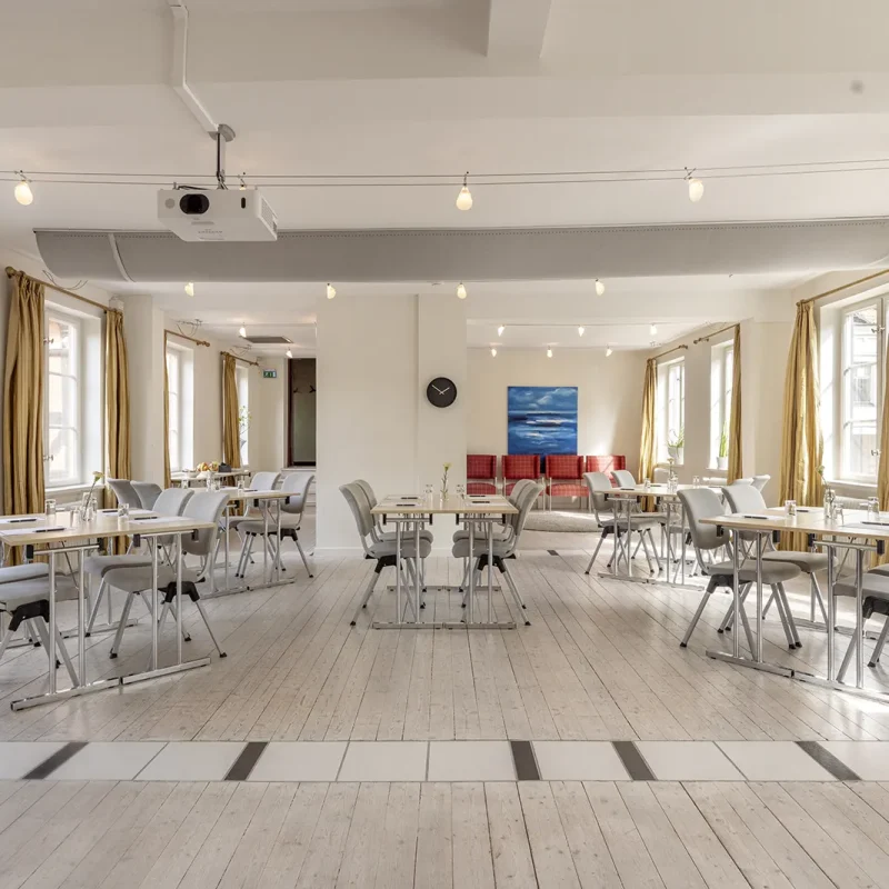 Margaretarummet med mötesbord i grupper, ljusa stolar, stora fönster och en takmonterad projektor.